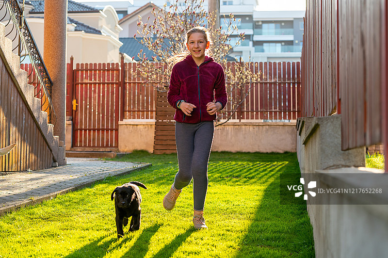 女孩和黑色拉布拉多小狗在后院奔跑图片素材