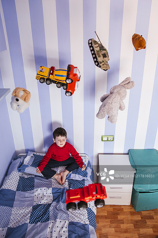小男孩在床上沉思，玩具在他头上飞来飞去图片素材