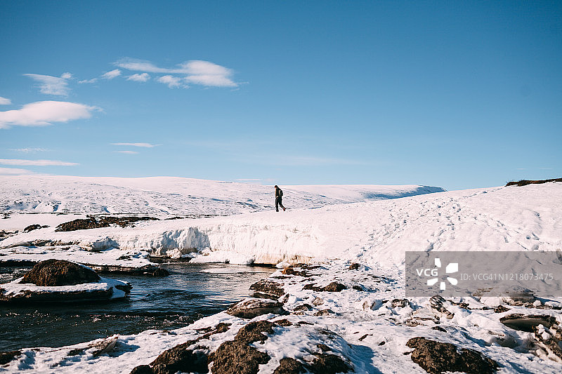 在阳光明媚的冬日里，在Godafoss瀑布附近的白雪皑皑的山前，一名男子向左转图片素材