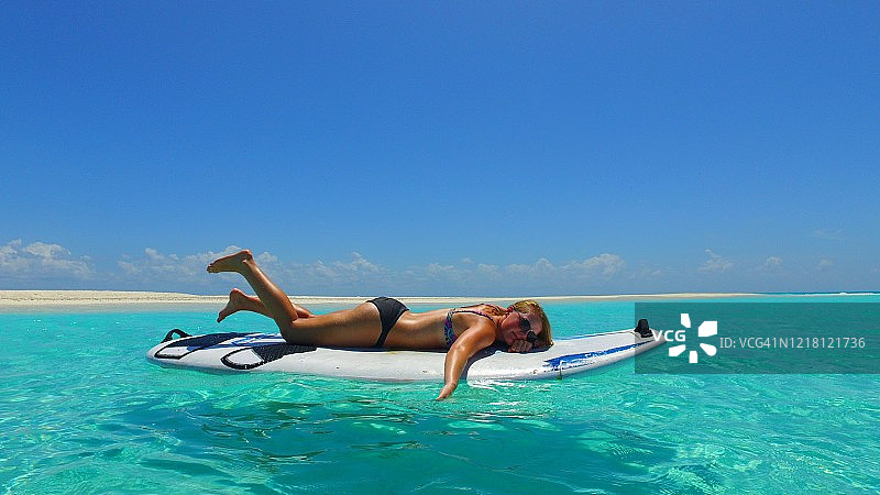 年轻的女士们喜欢在美丽的马尔代夫岛上玩桨板，那里有原始的海水和异国情调的白沙图片素材