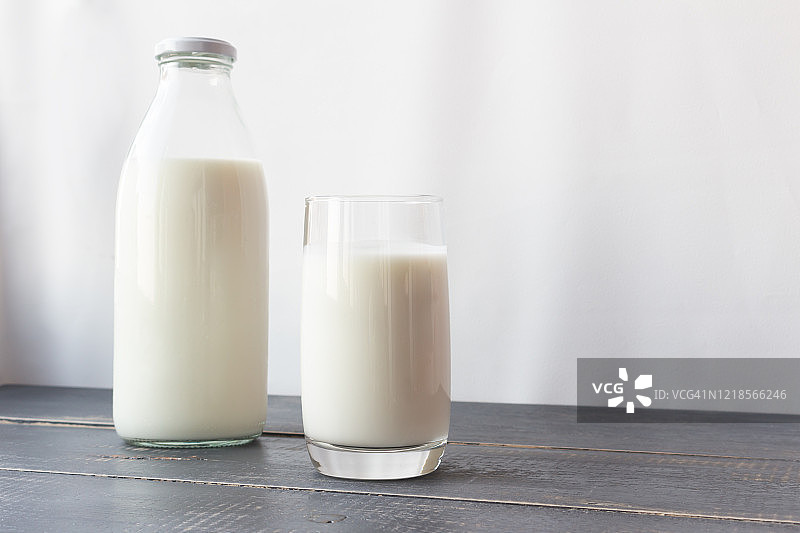发酵乳制品。牛奶，酸奶，玻璃瓶和玻璃杯。在灰色的木质背景上喝着农家酒。图片素材