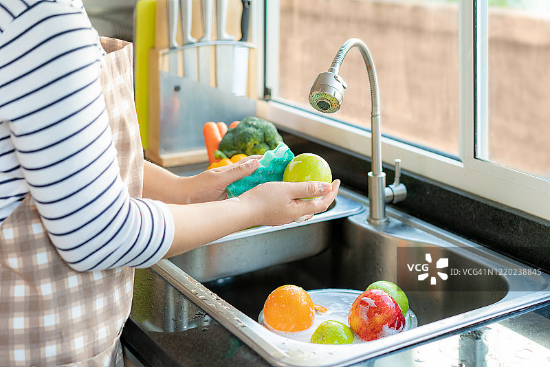 一名亚洲健康女性在厨房水槽上方清洗苹果和其他水果，并用肥皂涂抹水果/蔬菜，以消除感染COVID-19的可能性。图片素材