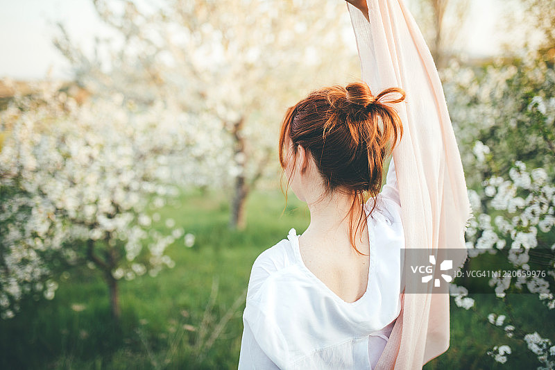 美丽的女人享受在鲜花盛开的田野的树木在日落。图片素材