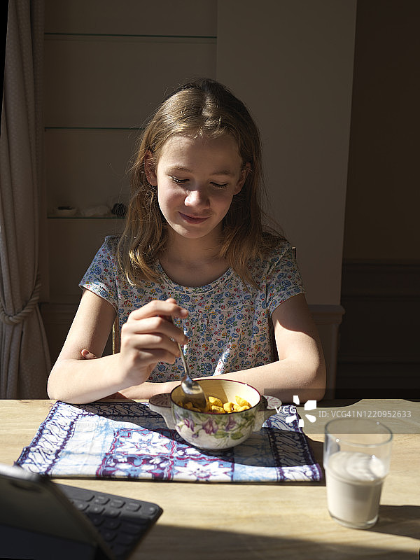 一个年轻的女孩一边吃早餐一边玩她的电子平板电脑，早上图片素材