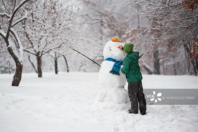 男孩站在森林里堆雪人，美国图片素材