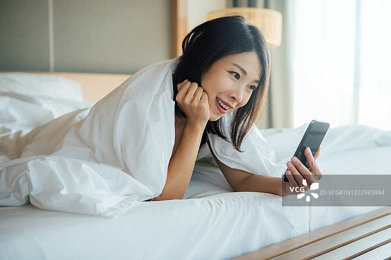 年轻女子在床上用智能手机打视频电话图片素材