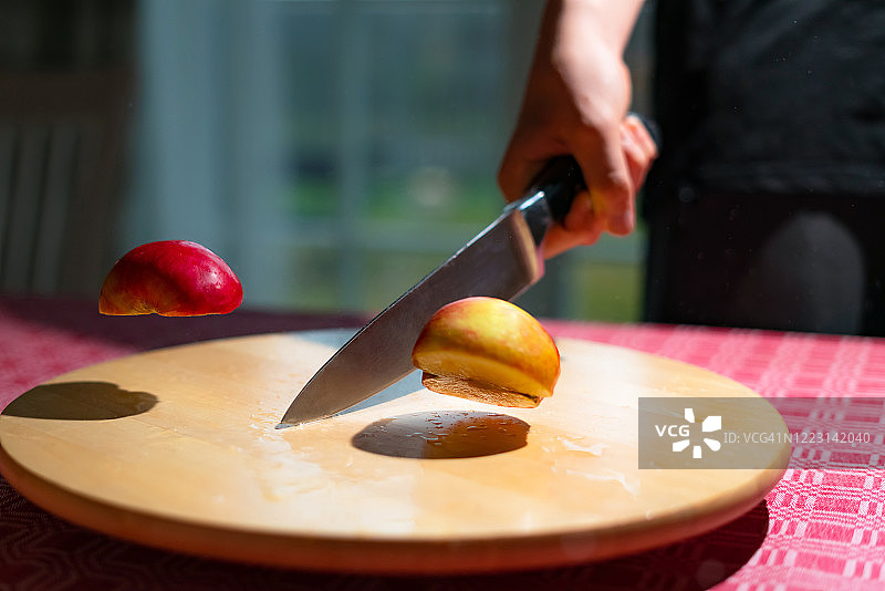 厨师用菜刀将苹果切成两半的特写。在木板上切红苹果图片素材