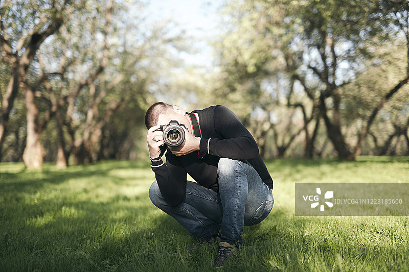 一名男子蹲在草地上用相机拍照图片素材