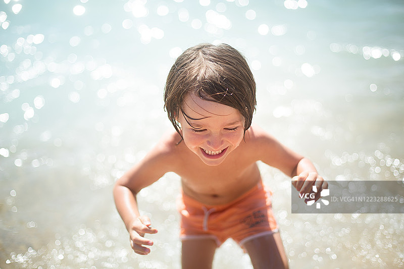 男孩微笑着从水里出来，在海滩上举起双臂图片素材