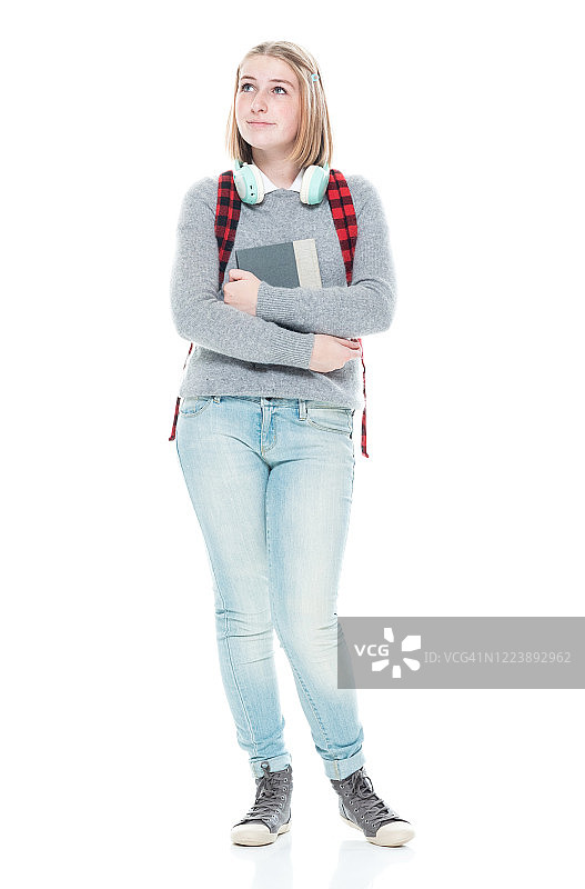 z一代年轻女性初中生站在白色背景前，穿着暖和的衣服，拿着书，戴着耳机图片素材