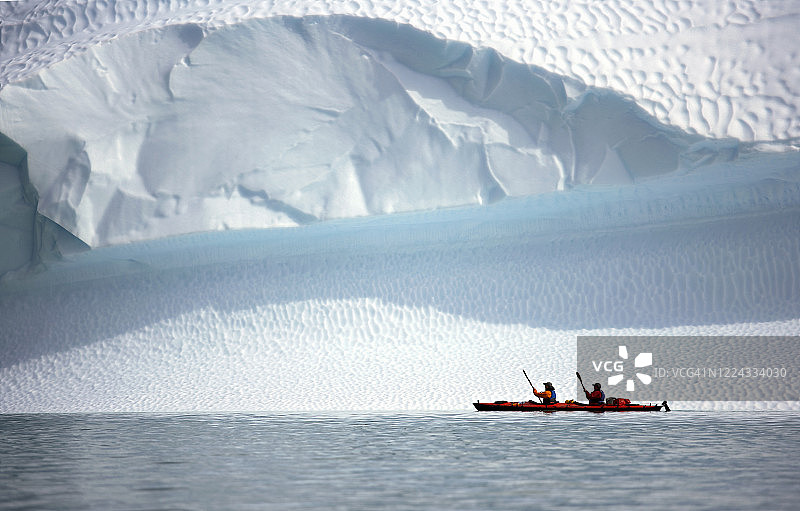两名男子在格陵兰岛的一座冰山上划着他们的海上皮划艇图片素材