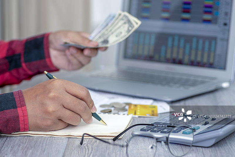 男人在手机上记录并计算每月用钞票支付信用卡债务的费用图片素材