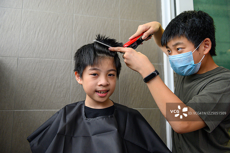 一个小男孩在禁闭期间在家给他弟弟理发图片素材