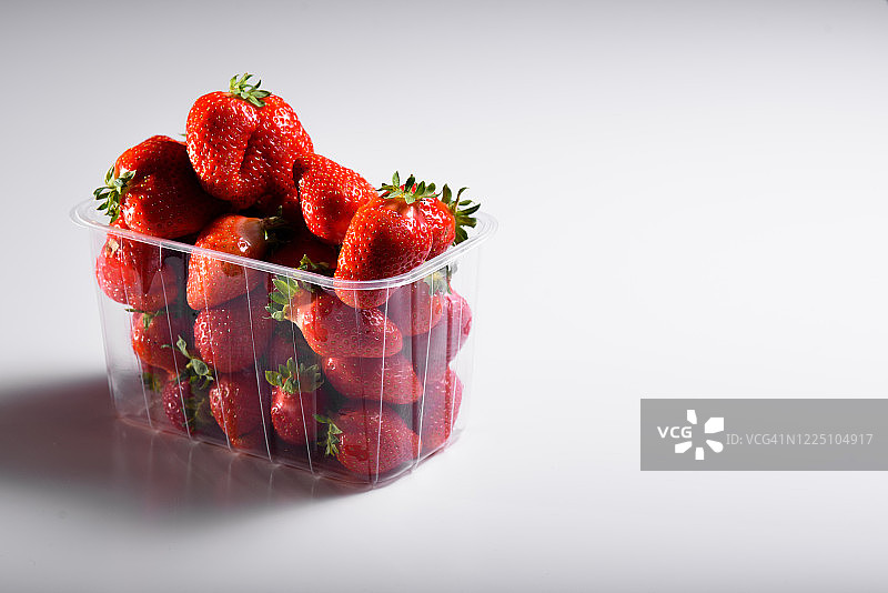 白色背景的塑料盒子里装着新鲜的有机草莓。有机产品的交付。有机草莓的包装。图片素材