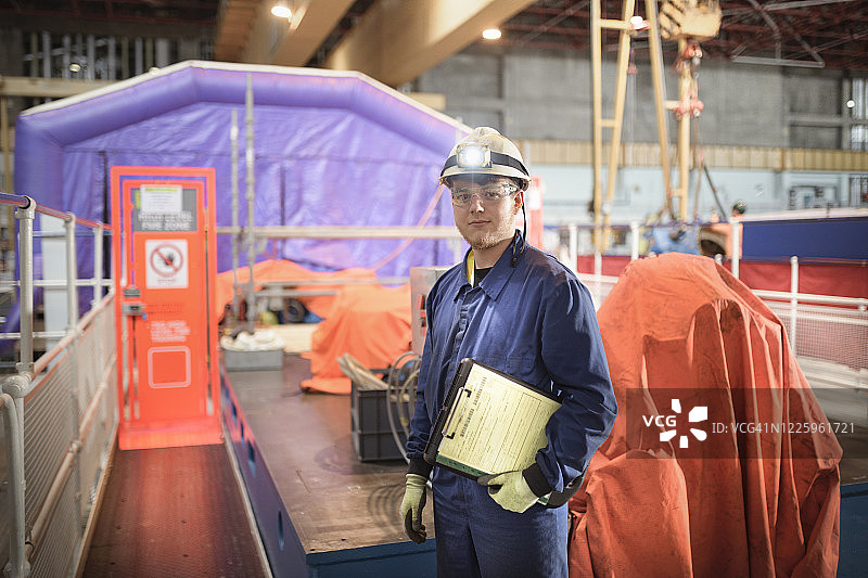 一位工程师站在核电站的涡轮大厅里，手里拿着剪贴板和笔记。图片素材