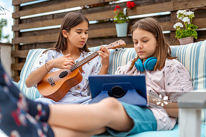 两个女孩拿着四弦琴、耳机和平板电脑在阳台上图片素材