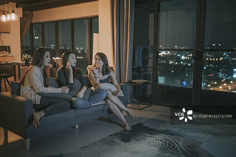 3个亚洲中国女人周五晚上聚集在公寓，看电视，看电影，坐在沙发上吃零食，享受每个公司图片素材
