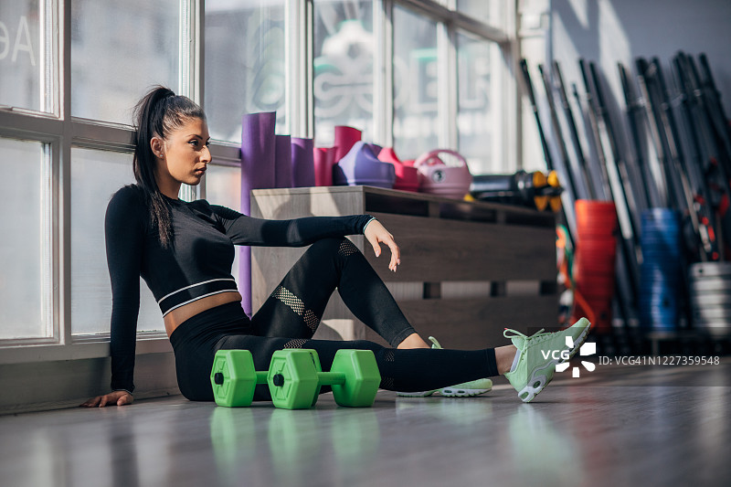 一个健康的女士独自坐在健身房的地板上图片素材
