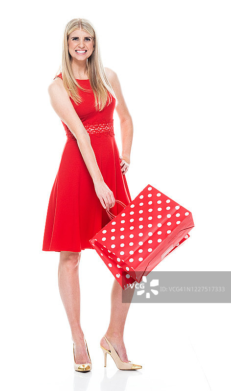 白种人年轻女性穿着裙子，拿着购物袋站在白色背景前图片素材
