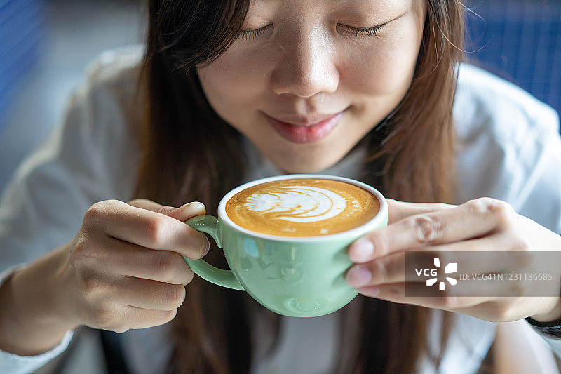 年轻的亚洲女人拿着一杯泡沫平坦的白咖啡与咖啡泡沫艺术图片素材