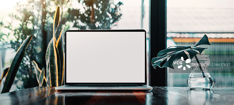 笔记本电脑空白屏幕上的桌子在咖啡馆的背景。笔记本电脑与空白屏幕上的咖啡店模糊背景。图片素材