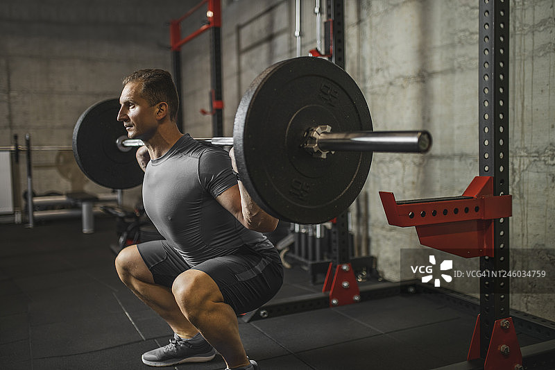 英俊的肌肉男在健身房用杠铃做下蹲锻炼图片素材