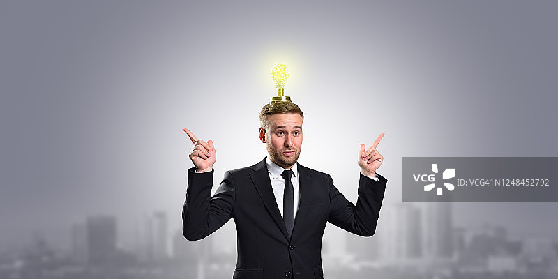 一个商人头顶上有一个灯泡，他的手指向一个灰色的背景和一个拷贝空间。经营理念理念创新。图片素材