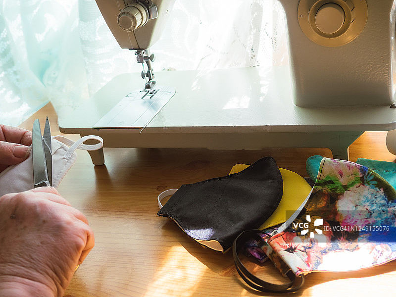 在新冠肺炎大流行期间，一名老年妇女在家里缝制可洗的布口罩图片素材