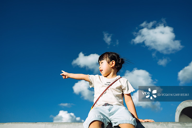 可爱的亚洲小女孩在户外公园玩，指着美丽的蓝天在一个可爱的阳光明媚的日子图片素材