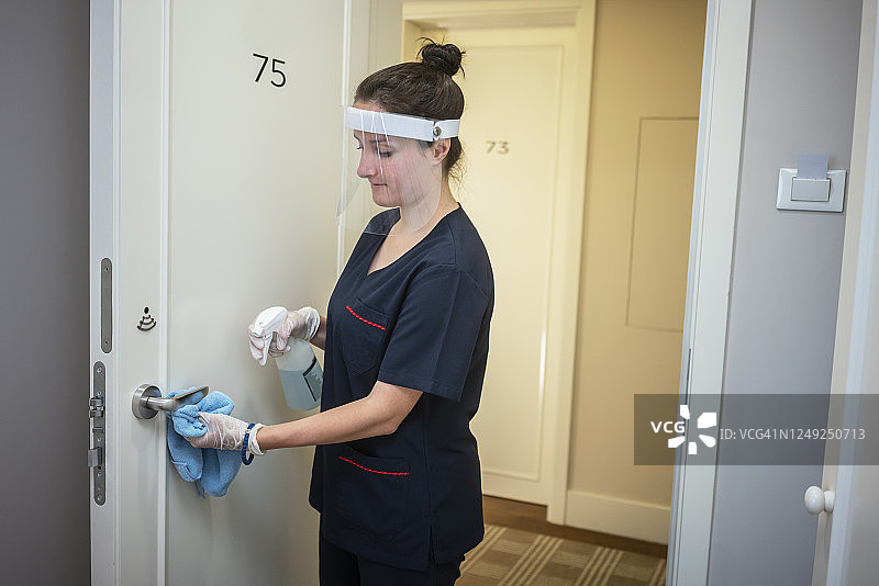 清洁门把手的服务员，在酒店工作时戴着口罩图片素材