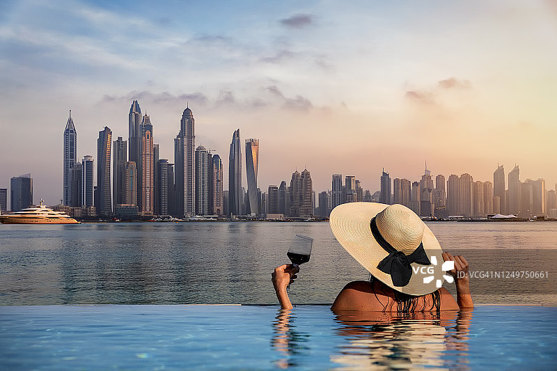 一位戴着帽子的妇女站在泳池边，欣赏着迪拜码头的天际线图片素材