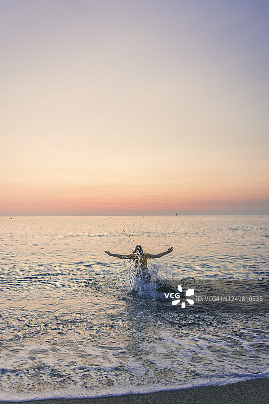 十几岁的女孩享受而溅水在海上在日出图片素材