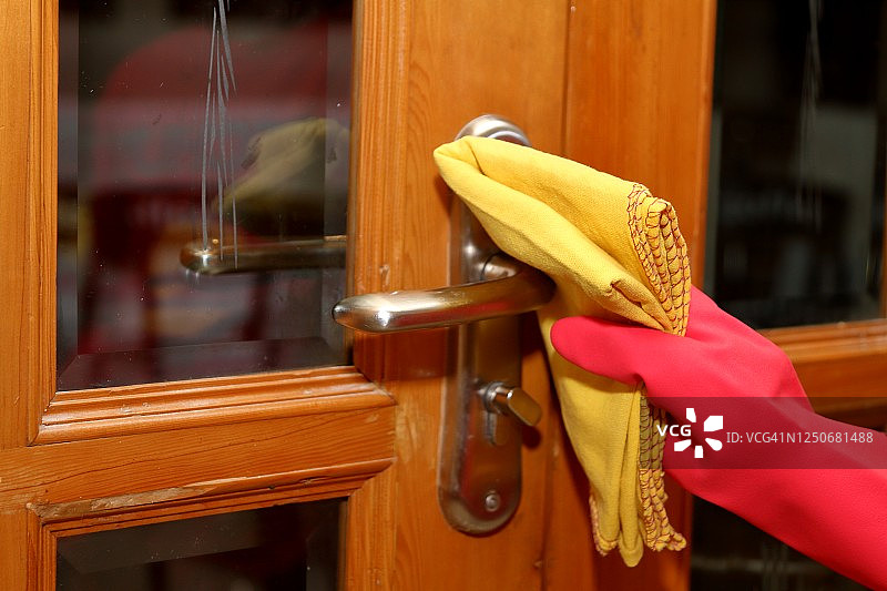 用黄色织物掸子清洁门把手，并戴上红色橡胶手套。图片素材