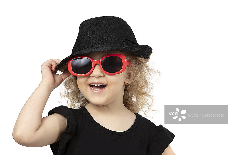 有趣的孩子。小女孩戴着黑色的帽子和太阳镜，背景是白色的。一个漂亮时尚的小女孩的肖像。四岁的金发婴儿。图片素材