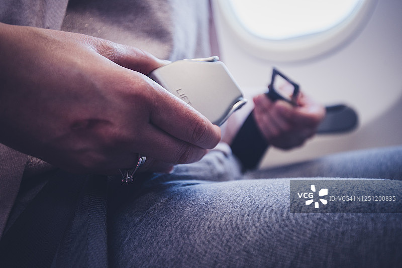 为了安全飞行，女性乘客坐在飞机上系好安全带。图片素材