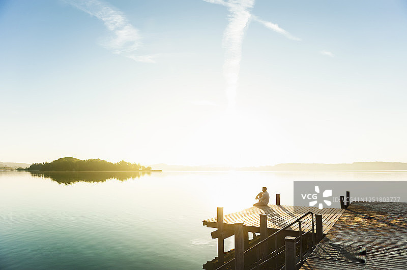一个年轻人坐在湖边的防波堤上欣赏日出图片素材