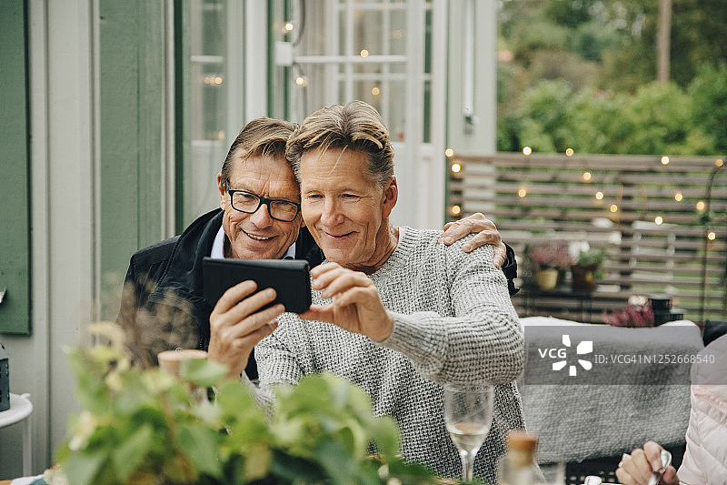 微笑的男人展示智能手机与朋友坐在后院聚会图片素材