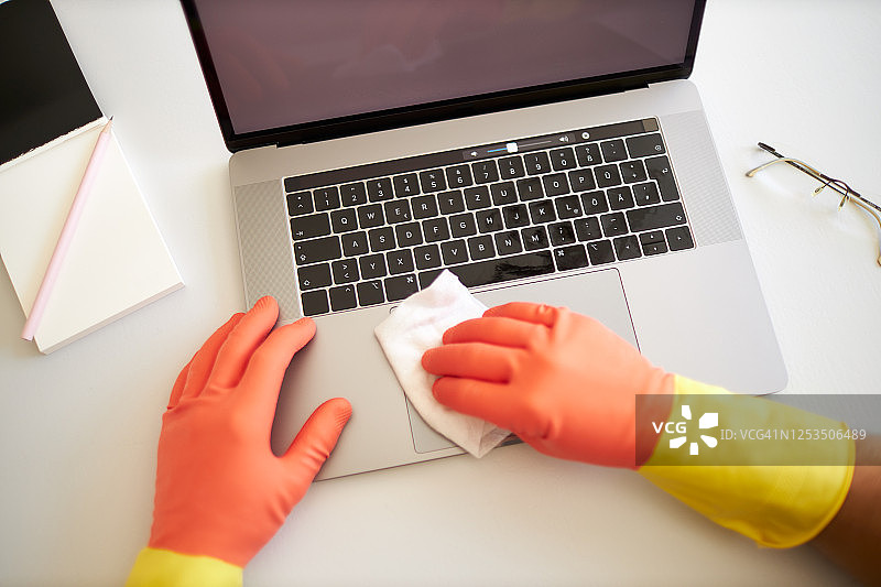 不同的照片，一男一女戴着橡胶手套，用消毒湿巾消毒和清洁笔记本电脑图片素材