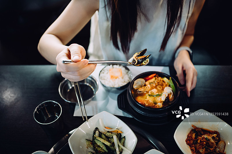 年轻的亚洲女人享受新鲜的传统韩式海鲜豆腐汤米饭和各种各样的开胃菜在韩国餐厅的镜头图片素材