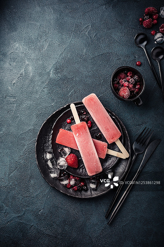 头顶拍摄自制冷冻冰棒与有机新鲜浆果，覆盆子，草莓，加仑子，蓝莓在黑色的盘子。图片素材