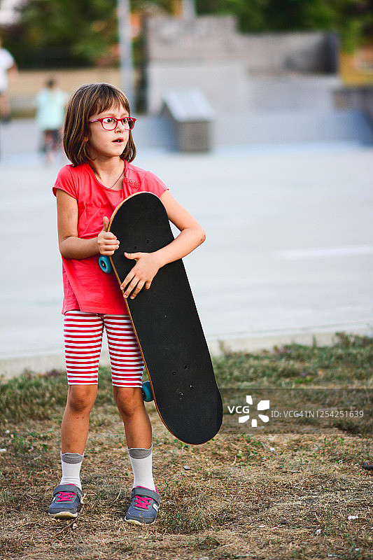可爱的小女孩拿着滑板在城市里。图片素材