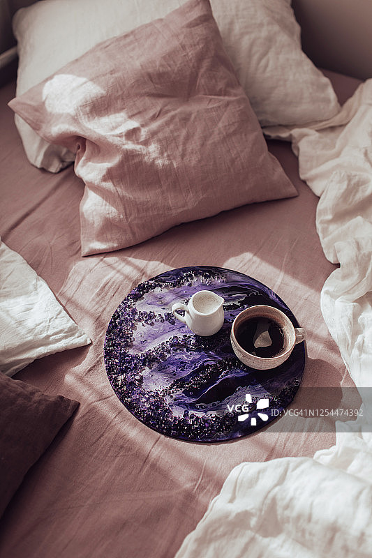 手工水晶紫环氧树脂装饰托盘和咖啡杯在粉红色和白色的床上。液态大理石纹理-液态艺术装饰。现代潮流的艺术作品。图片素材