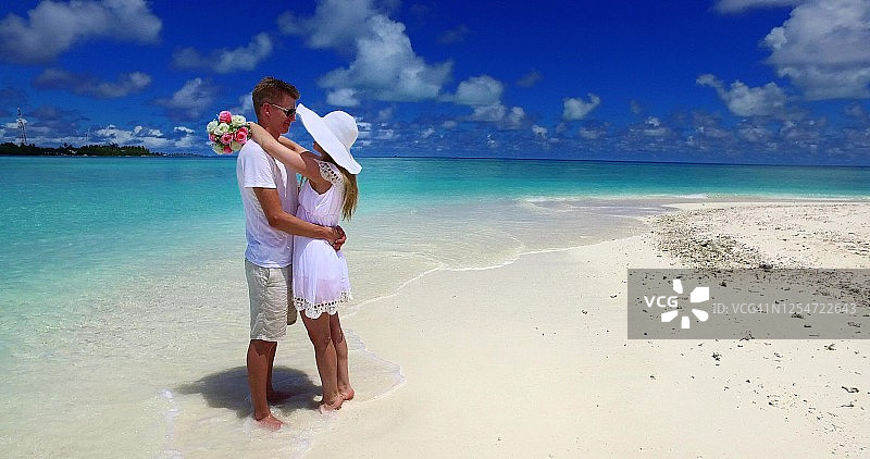 在异国情调的海滩上，一对穿着白衣的年轻夫妇在交谈图片素材