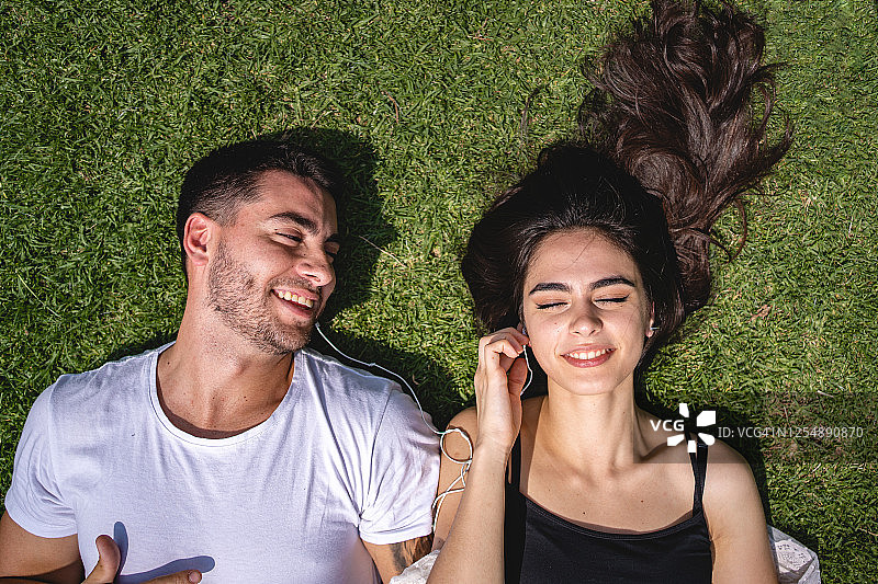 一对年轻的情侣躺在公园里听着音乐坠入爱河图片素材