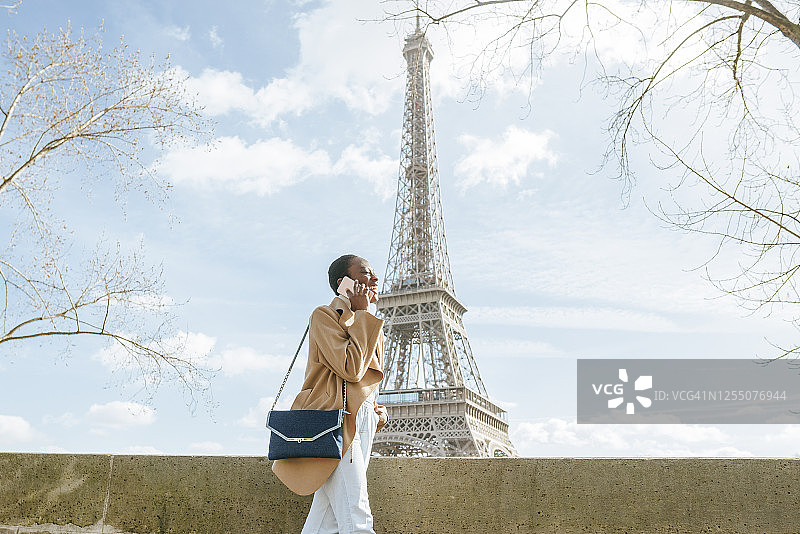 法国巴黎，一名年轻女子在以埃菲尔铁塔为背景的桥上玩手机图片素材