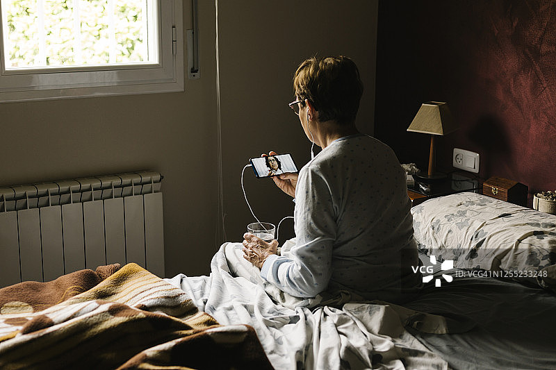 一位退休妇女坐在家里的卧室里与医生进行视频通话图片素材