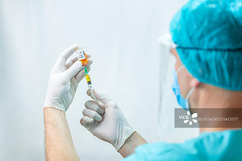 医生戴着外科手套，使用注射器从药瓶中取出COVID-19疫苗图片素材