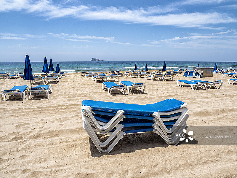 在西班牙贝尼多姆的莱万特海滩上，海滩伞和太阳躺椅对着蓝天。图片素材