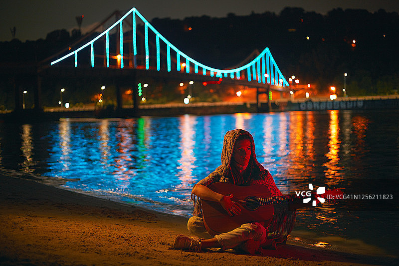 一个嬉皮女人晚上在街上弹原声吉他。图片素材