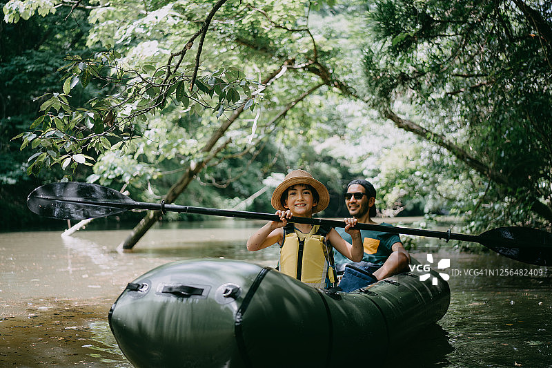 快乐的女孩和父亲划着小舟穿过森林里的河流图片素材